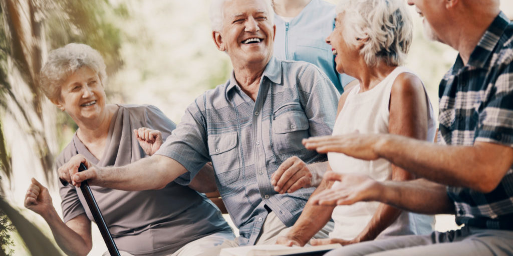 Happy elderly man with walking stick and smiling senior people relaxing in the garden