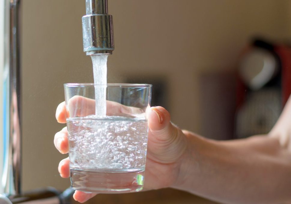 Woman filling a glass of water from a stainless steel or chrome tap or faucet, close up on her hand and the glass, half full