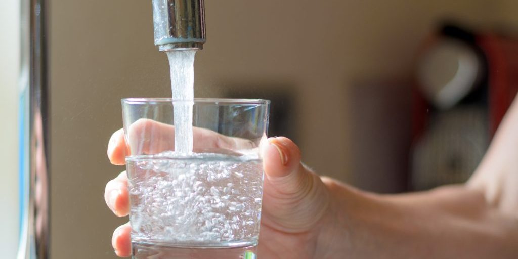 Woman filling a glass of water from a stainless steel or chrome tap or faucet, close up on her hand and the glass, half full