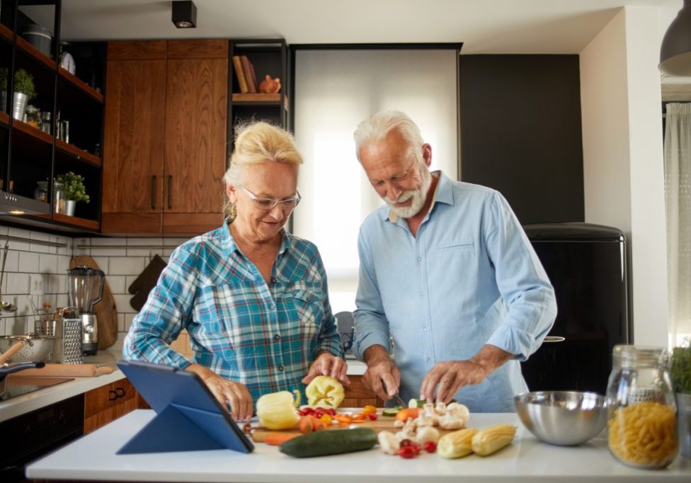 Cheerful senior couple preparing healthy meal using online recipe