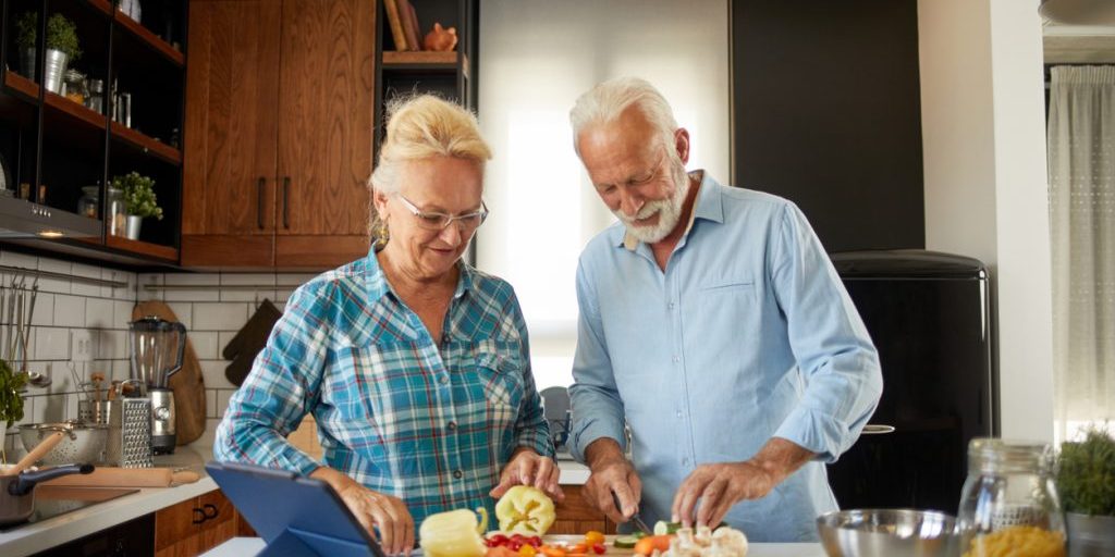 Cheerful senior couple preparing healthy meal using online recipe